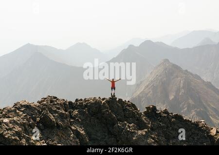 Frau, die mit ausgestreckten Armen auf dem Gipfel des Berges steht Der Himmel ist klar Stockfoto