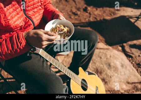 Niedriger Abschnitt des Mannes, der Nahrung hat, während er mit Gitarre sitzt Im Canyonlands National Park Stockfoto