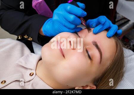 Gesicht einer schönen Frau mit buschigen Augenbrauen in einem Schönheitssalon. Dauerhafte Make-up für Augenbrauen. Kosmetikerin macht Augenbraue Tattoo für Frauen. Beauty-Prozess Stockfoto