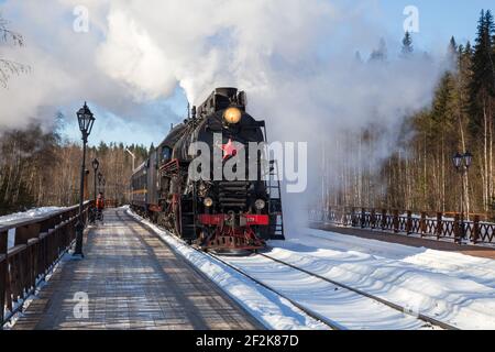 RUSKEALA, RUSSLAND - 10. MÄRZ 2021: Tourist retro Zug Ruskeala Express auf Dampflokomotive kommt an der Station Gorny Park Ruskeala Stockfoto