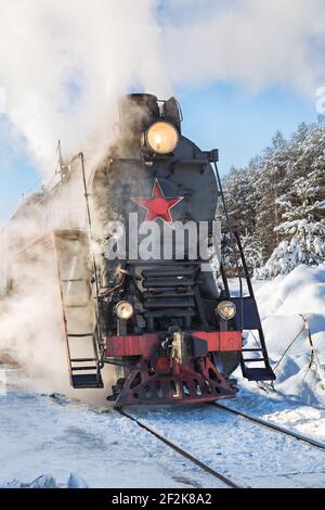 Alte Dampflokomotive raucht Dampffahrten in einem verschneiten Wald Stockfoto