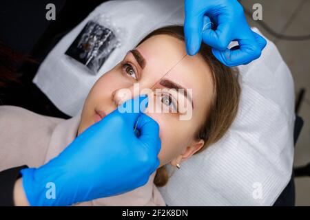 Frau mit Permanent Make-up Tattoo auf ihren Augenbrauen. Nahaufnahme Kosmetikerin macht eine Skizze der Augenbrauen. Professionelles Make-up und kosmetische Hautpflege. Stockfoto