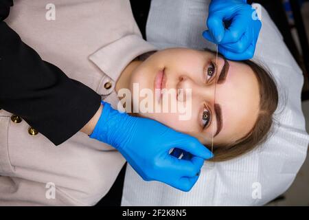 Frau mit Permanent Make-up Tattoo auf ihren Augenbrauen. Nahaufnahme Kosmetikerin macht eine Skizze der Augenbrauen. Professionelles Make-up und kosmetische Hautpflege. Stockfoto