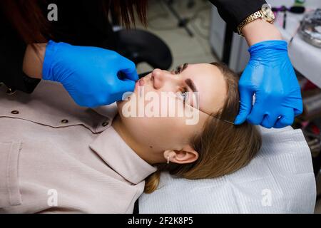 Frau mit Permanent Make-up Tattoo auf ihren Augenbrauen. Nahaufnahme Kosmetikerin macht eine Skizze der Augenbrauen. Professionelles Make-up und kosmetische Hautpflege. Stockfoto