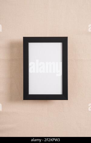 Schwarzer Bilderrahmen mit weißem Mockup auf beigefarbenem Textil Stockfoto