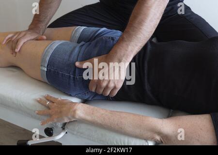 Hände des Phisiotherapeuten auf Hüfte und linkes Knie der Patientin, die auf der Bahre liegt. Anonymer Osteopath, der Frau mit Körperverletzung behandelt Stockfoto
