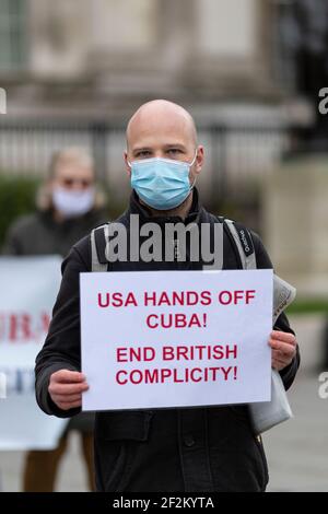 Portrait eines Protesters in Gesichtsmaske mit Plakat, bei Demonstration gegen US-Beteiligung in Kuba, Trafalgar Square, London, 12. Dezember 2020 Stockfoto