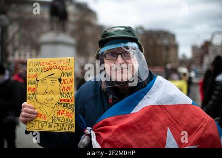 Protestant in Gesichtsschild mit Plakat und mit kubanischer Flagge drapiert, bei Demonstration gegen US-Beteiligung in Kuba, Trafalgar Square, London, 12. Dezember Stockfoto