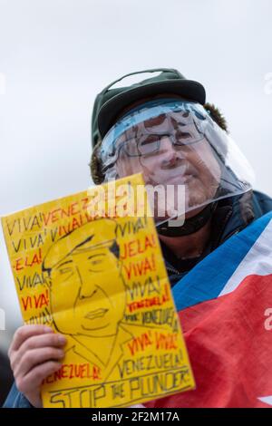 Protestant in Gesichtsschild mit Plakat und mit kubanischer Flagge drapiert, bei Demonstration gegen US-Beteiligung in Kuba, Trafalgar Square, London, 12. Dezember Stockfoto