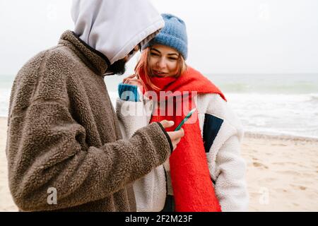 Schönes junges Paar mit Handy am Strand tragen Kalte Kleidung Stockfoto