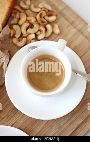 Tasse frisch gebrühter Espresso auf Holzbrett mit Cashewnüssen. Stockfoto