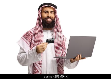 Saudi-arabischer Mann mit Kreditkarte und Laptop Computer, der die Kamera isoliert auf weißem Hintergrund betrachtet Stockfoto