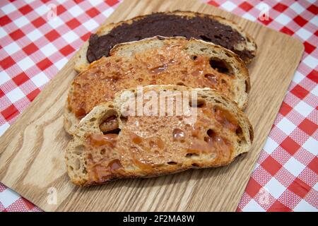 Köstliche Scheiben von braunem Toast mit Marmelade und Schokolade bedeckt Auf einem Holzbrett auf einem Küchentisch zum Frühstück verteilen Stockfoto