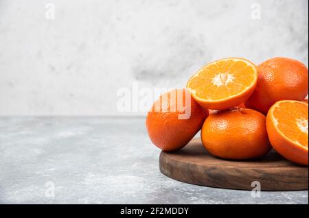 Ein Holzbrett voller saftiger Orangenfrüchte mit Scheiben Auf steinernem Hintergrund Stockfoto