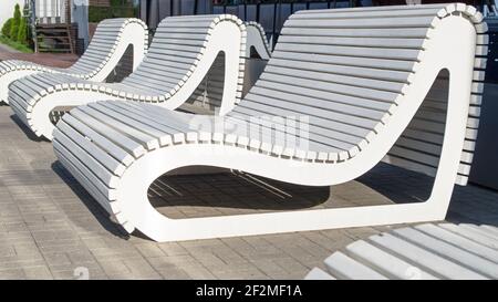 Eine Reihe von weißen Holz ungewöhnliche Bänke von modernem Design, stromlinienförmige abgerundete Form, erinnert an eine Strandliege in der Gegend mit Beschichtung Fliesen auf Th Stockfoto