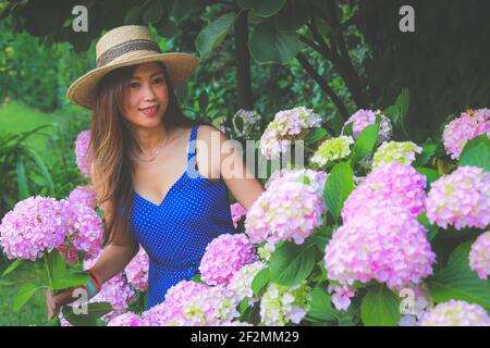 Asiatische Frau trägt Strohhut stehen mit rosa Hortensien Blumen Im Garten Stockfoto