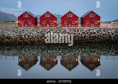 Klassische rote Fischerhütten in perfekter Symmetrie, die an einem Steinsteg mit einer leicht verschwommenen Spiegelung sitzen. Klassische rote Häuser von nordnorwegen Stockfoto