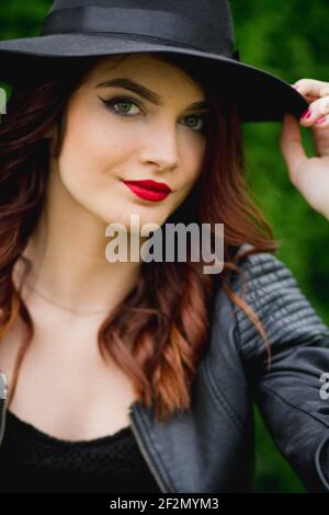 Ein Porträt einer stilvollen Frau in einer Lederjacke Gepaart mit einem Fedora Hut in einem Park Stockfoto