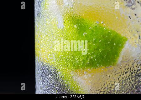 Eine Scheibe Limettenfrucht in einem kohlensäurehaltigen Wasser, auf schwarzem Hintergrund Stockfoto