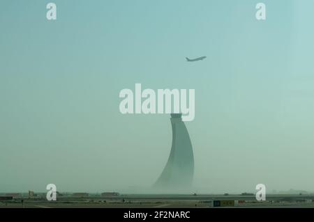 Flugzeug, das über den gekrümmten Kontrollturm des abu dhabi Flughafens fliegt. Unter dem Turm ist Nebel Stockfoto