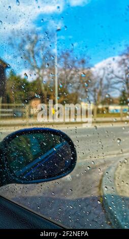 An sonnigen Tagen fällt Wasser auf die Windschutzscheibe. Blick auf die Straße durch das Fensterglas des Autos von Regentropfen bedeckt Stockfoto
