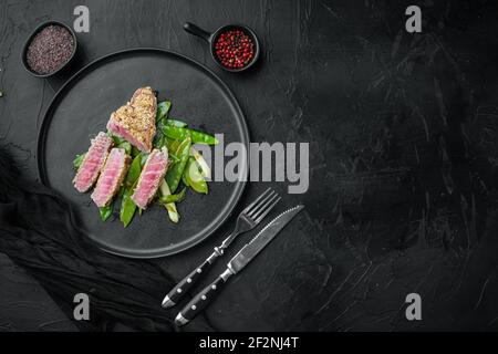 Thunfisch Tataki Sesamkruste Vorspeise Set mit Frühlingszwiebeln und Zuckererbsen, auf Teller, auf schwarzem Stein Hintergrund, Draufsicht flach legen, mit Copyspace Stockfoto