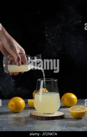 Eine Hand gießt Zitronensaft in eine Glastasse Stockfoto