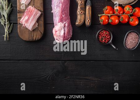 Frisches und rohes Fleisch. Ganzes Stück Schweinefilet Sirloin mit Zutaten und Kräutern zum Grillen oder Backen, Salbei, Kartoffel-Set, auf schwarzem Holztisch backgr Stockfoto