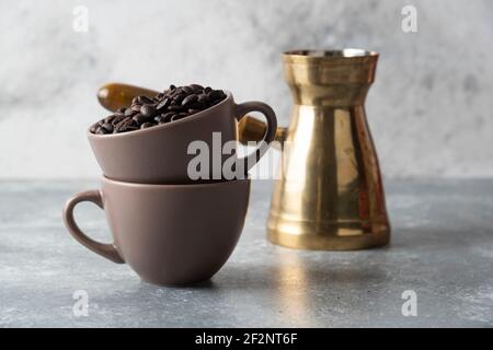 Tasse voll mit Kaffeebohnen und Kaffeemaschine auf Marmor Hintergrund Stockfoto