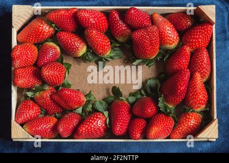 Overhead-Ansicht eines Holztablett mit einem Raum Kopie in der Mitte von frischen Erdbeeren auf einem blauen Stoff Textur Hintergrund umgeben. Gesunde Ernährung. Stockfoto