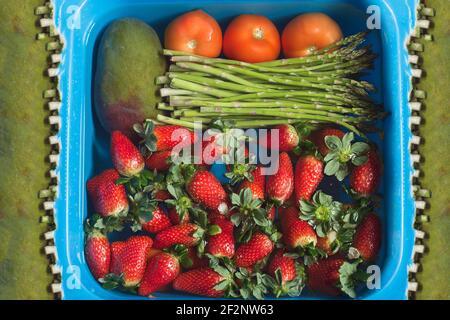 Eine blaue Schüssel gefüllt mit Obst und Gemüse in Wasser getaucht mit Bleichmittel, um Lebensmittel auf einem abstrakten Hintergrund mit organischer Textur zu desinfizieren. Stockfoto