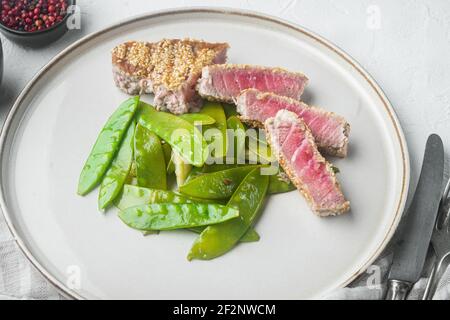 Thunfisch-Braten in Sesam-Set mit Frühlingszwiebeln und Zuckererbsen, auf Teller, auf weißem Steingrund Stockfoto