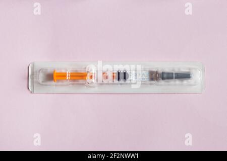 Einzeln versiegelte Spritze mit einer medizinischen Lösung in einem Kunststoff-Blister auf einem strukturierten rosa Papier Hintergrund vorgefüllt. Wissenschaft Gesundheit und Medizin. Stockfoto