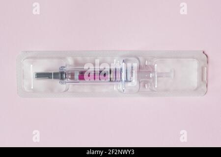 Einzeln versiegelte Spritze mit einer medizinischen Lösung in einem Kunststoff-Blister auf einem strukturierten rosa Papier Hintergrund vorgefüllt. Wissenschaft Gesundheit und Medizin. Stockfoto