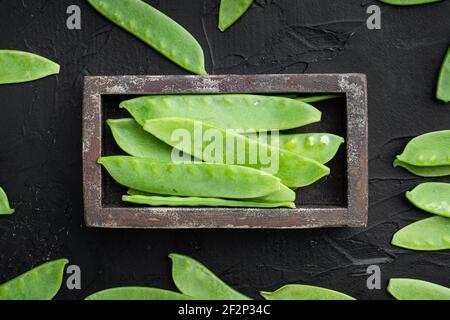 Frische Bio-Mangout, auch bekannt als Zucker Snap Erbsenset, in Holzkiste, auf schwarzem Stein Hintergrund, Draufsicht flach legen Stockfoto