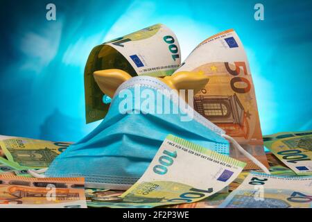 Sparschwein mit blauem Mund- und Nasenschutz und Euro-Banknoten vor blauem Hintergrund. Stockfoto