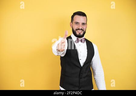 Junger Mann mit Bart in Fliege und Weste lächelnd Freundlich bietet Handschlag als Begrüßung und einladend Stockfoto