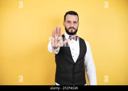 Junger Mann mit Bart tragen Fliege und Weste ernst und tun aufhören zu singen mit Handfläche der Hand. Stockfoto