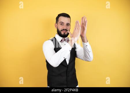 Junger Mann mit Bart in Fliege und Weste klatschen und applaudieren glücklich und fröhlich, lächelnd stolze Hände zusammen Stockfoto