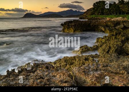 Spektakulärer Sonnenuntergang in Paradise Cove, Wellen des Pazifischen Ozeans, die auf vulkanischen Felsen entlang der idyllischen Küste, Kapolei, Oahu, Hawaii, USA, krachen Stockfoto