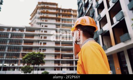 Thema ist der Gesundheitsschutz in Produktion und Bau. Kaukasische männliche Arbeiter in orange Uniform und Schutzmaske kn 95 setzt auf Stockfoto