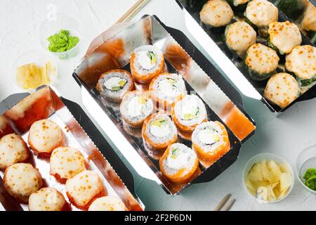 Leckere Sushi-Rollen in Einwegboxen Set, auf weißem Stein Hintergrund Stockfoto