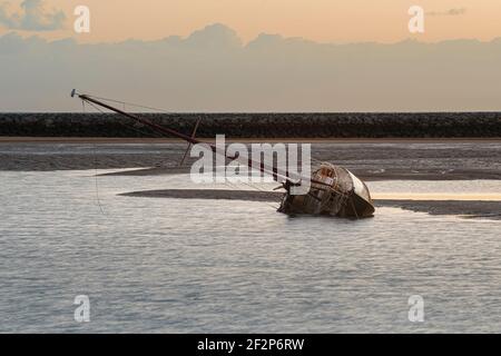 Eine verlassene Yacht liegt auf ihrer Seite, auf Grund im Hafen bei Ebbe. Stockfoto