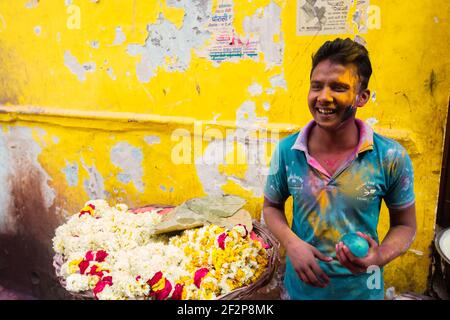 Indien Vrindavan junger Mann bedeckt mit farbigem Pulver verkauft Blumen halten Wasserballon bereit, Holi zu spielen. Stockfoto