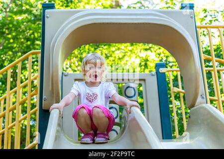 Kleines glückliches Kind auf einer Rutsche auf einem Spielplatz in Der Park an einem sonnigen Sommertag Stockfoto
