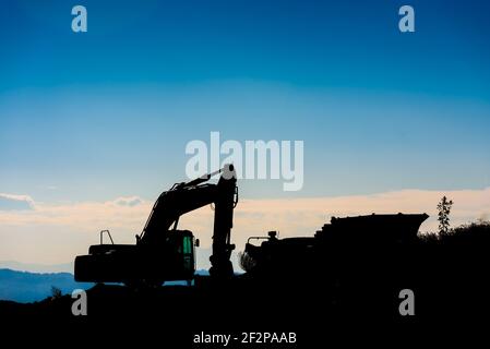 Hinterleuchtete Silhouette eines Baggers auf einem Hügel mit unfokussierten Himmel Hintergrund. Stockfoto