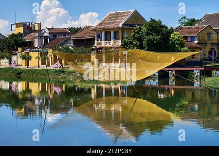 Großes gelbes Fischernetz, das über dem Thu Bon River schwebt, und gelbe, pastellfarbene Häuser im Hintergrund am Fluss Hoi Ann Old Town, Vietnam Stockfoto