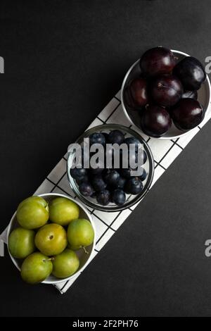Schwarze und grüne Pflaumen in weißer Keramik-Untertasse, Draufsicht Stockfoto