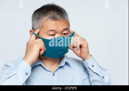 Asiatischer Mann mittleren Alters trägt auf einer wiederverwendbaren Polyurethan-Gesichtsmaske zum Schutz vor Covid-19. Isoliert auf weißem Hintergrund. Stockfoto