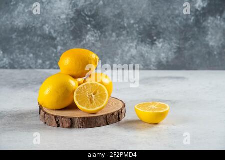 Zitronenscheiben in Holzbrett mit einer ganzen Zitrone auf Marmorhintergrund Stockfoto